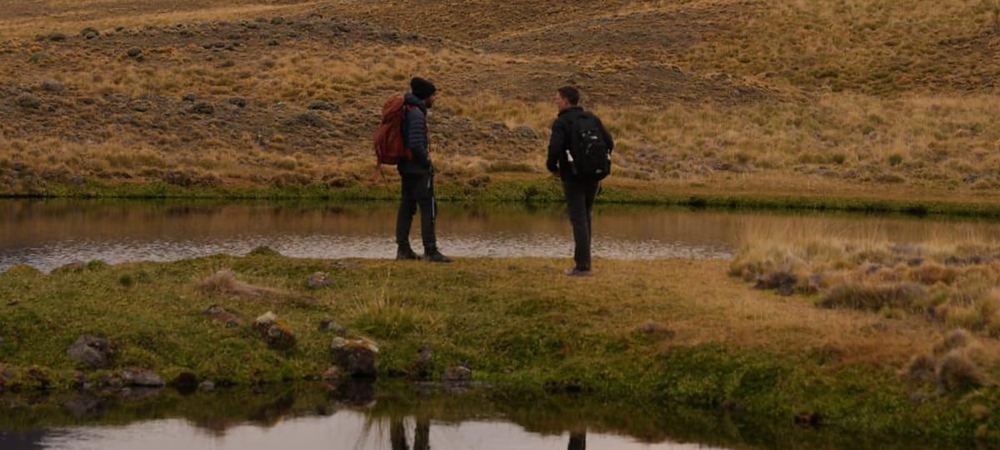 Dos personas frente a una laguna en la Patagonia, con montañas al fondo